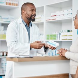 Healthcare, pharmacist and woman at counter with medicine or prescription drugs in hands at drug store. Health, wellness and medical insurance, man and customer at pharmacy for advice and pills.