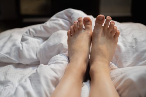 Two leg of pretty girl on white bed.part of the girl's legs stick out from under the blanket, rest
