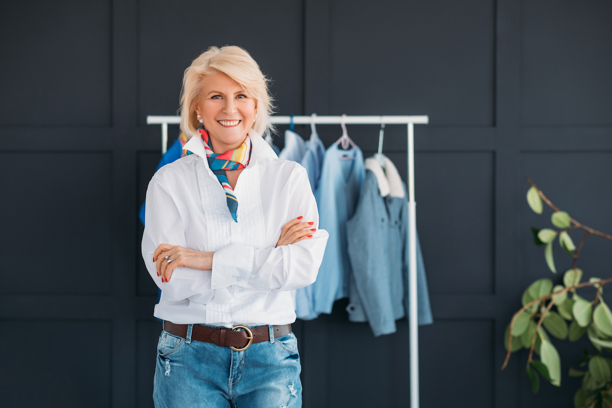 Fashionable mature woman standing in front of a rack of clothing wearing jeans and a white shirt