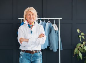 Fashionable mature woman standing in front of a rack of clothing wearing jeans and a white shirt