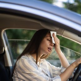 Girl driver being hot during heat wave in car, suffering from hot weather, has problem with a non-working air conditioner, wipes sweat from her forehead with tissue. Summer, heat concept.
