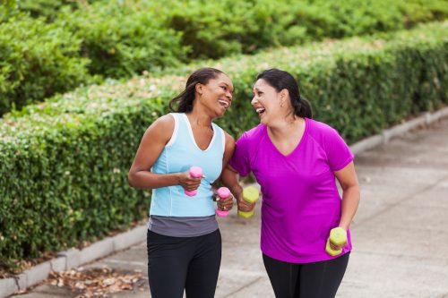 Female friends on an outdoor walk carrying light hand weights and laughing