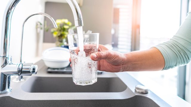 Close up of a person filling a glass with tap water from a sink faucet