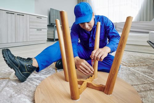 Handyman using screwdriver when assembling wooden table in apartment of customer