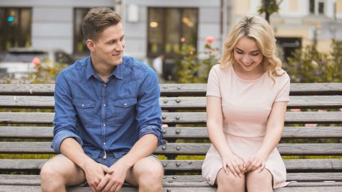 man flirting with blonde woman on a park bench