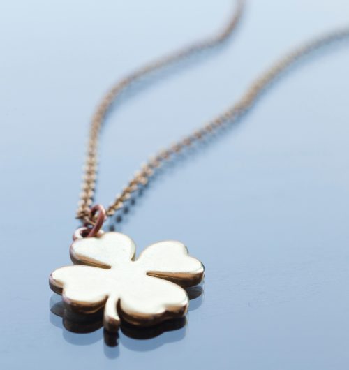 Gold four-leaf clover charm necklace on a pale blue background