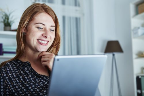 Woman smiling as she reads through congratulations messages on her laptop