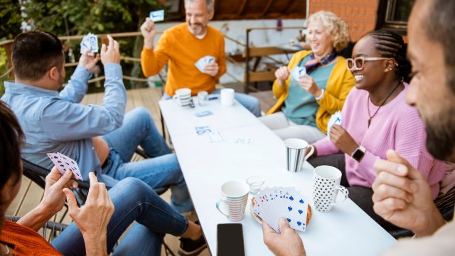 A group of friends of different ages sitting around a patio table playing cards and laughing.