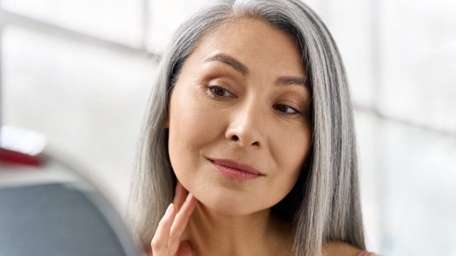 woman admiring herself in the mirror after researching hacks for how to look younger
