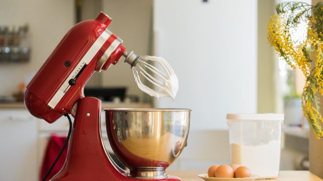 A red KitchenAid stand mixer in the up position with a bowl below the whisk