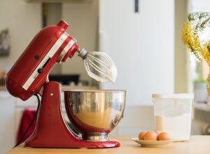 A red KitchenAid stand mixer in the up position with a bowl below the whisk