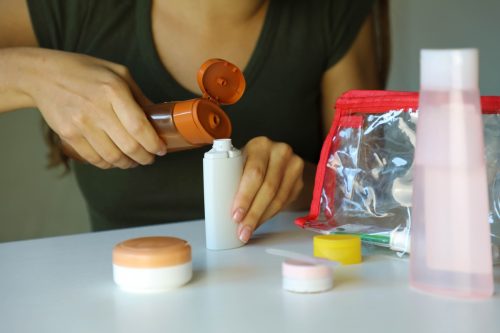 Woman poured liquid into small bottles preparing travel kit for transporting on airplane. Travel kit transporting cosmetics on airplane concept.