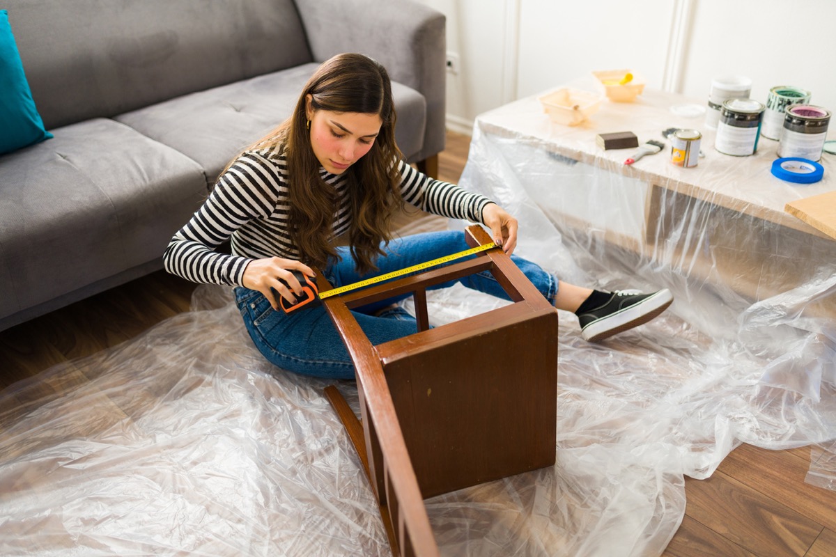 woman measuring a chair while working on a furniture flipping project at home