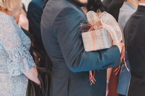 Close up of a man in a suit standing in a ceremony aisle holding a wedding gift