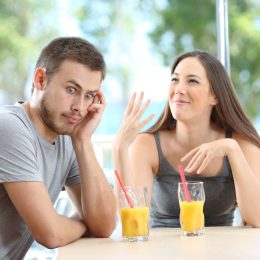 Man looking away and rolling his eyes at a talkative woman while at a restaurant table having orange juice.