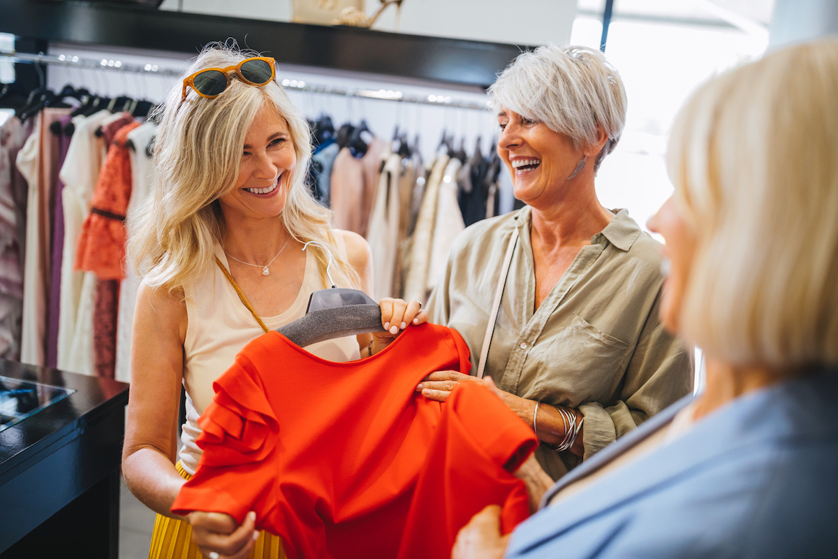 Three mature female friends laughing and having a good time while clothes shopping.