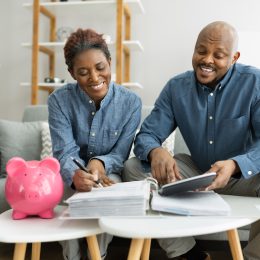 Middle-aged couple sitting on their couch planning for retirement with a pink piggy bank on the table