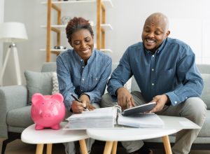 Middle-aged couple sitting on their couch planning for retirement with a pink piggy bank on the table