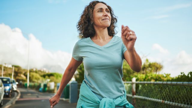 Mature woman in seafoam green sportswear smiling while out for a power walk in summer