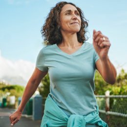 Mature woman in seafoam green sportswear smiling while out for a power walk in summer