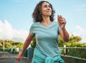 Mature woman in seafoam green sportswear smiling while out for a power walk in summer
