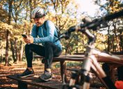 male cyclist sitting on a bench in the forest playing offline games on his phone