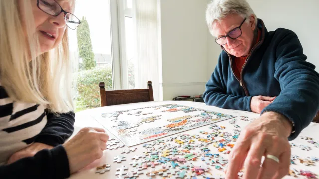 An older couple does a jigsaw puzzle at the kitchen table.
