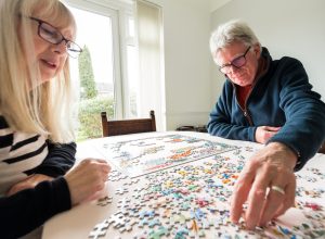 An older couple does a jigsaw puzzle at the kitchen table.