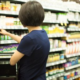 Woman Shopping at Grocery Market Pharmacy. Supermarket Shopper Doing Groceries. Female Holding Basket Trying to Decide which Products to Buy. Retail Healthcare Medicine, Vitamins, and Supplements.