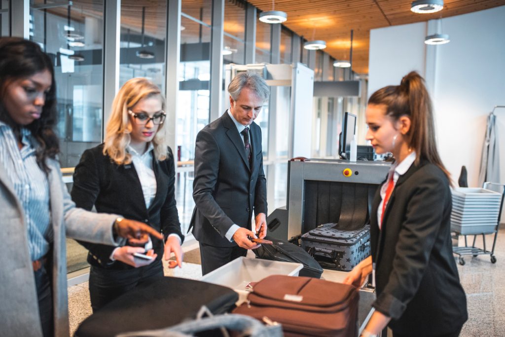 Travelers placing their items and luggage through an airport security checkpoint x-ray machine