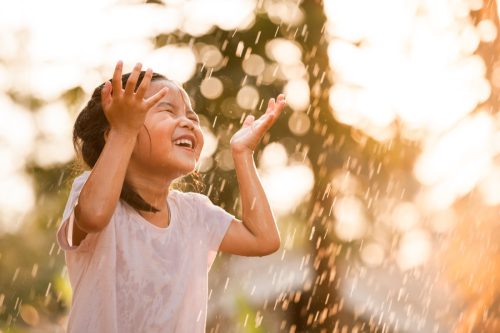 little girl smiling as she dances in the rain