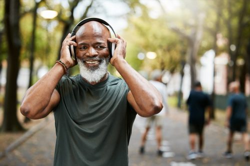 Man in park smiling and holding his headphones against his ears