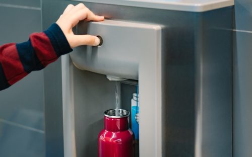 Hand of a traveler pressed the button of drinking water filling station at the Airport, Refill, Reusable bottle. Eco friendly, Environmental awareness, Clean water, Zero waste, Plastic free july.