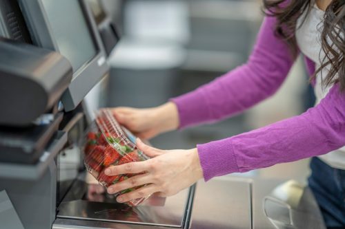 A photo showing a woman's hands scanning a box of strawberries at the grocery store's self check out service.