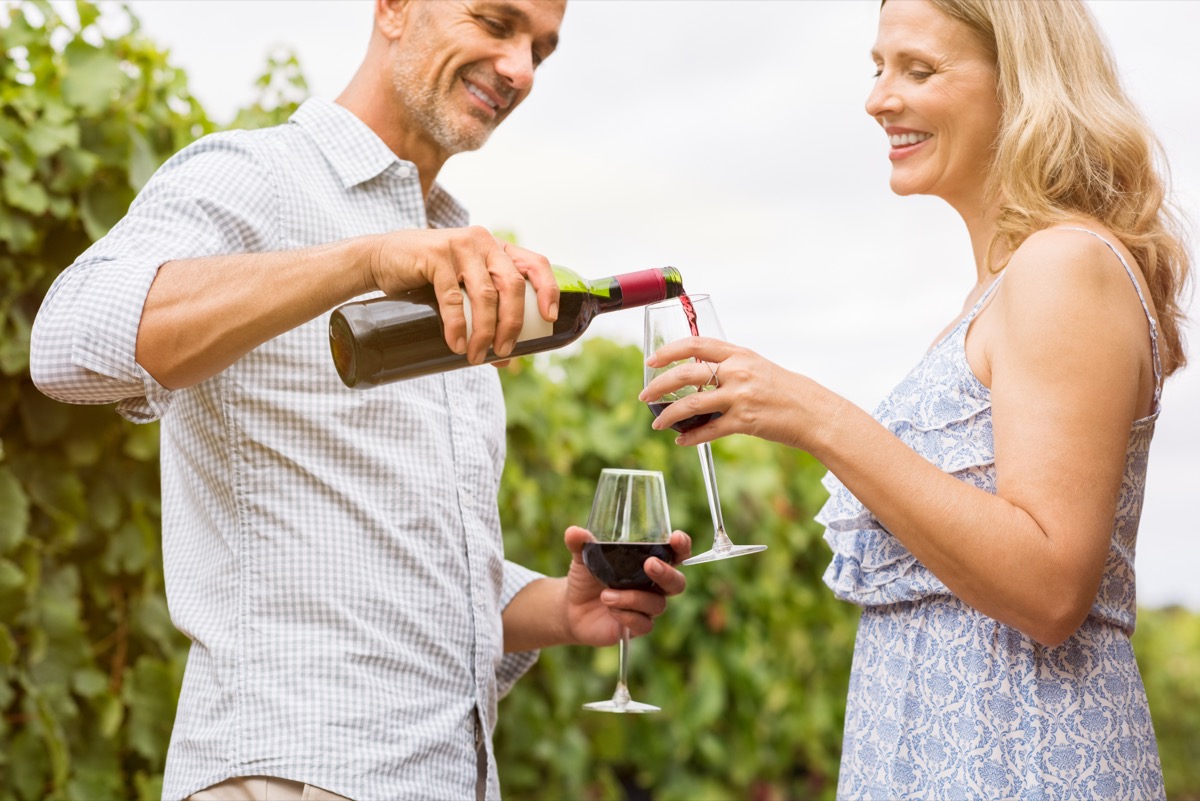 Mature man pouring red wine in glasses for celebrating anniversary with his wife. Happy mature couple in vineyard witha botlle of wine. Smiling mature couple drinking red wine in a vineyards.