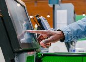 man finger touches screen of self-pay point to pay in shopping mall supermarket light hall extreme close view