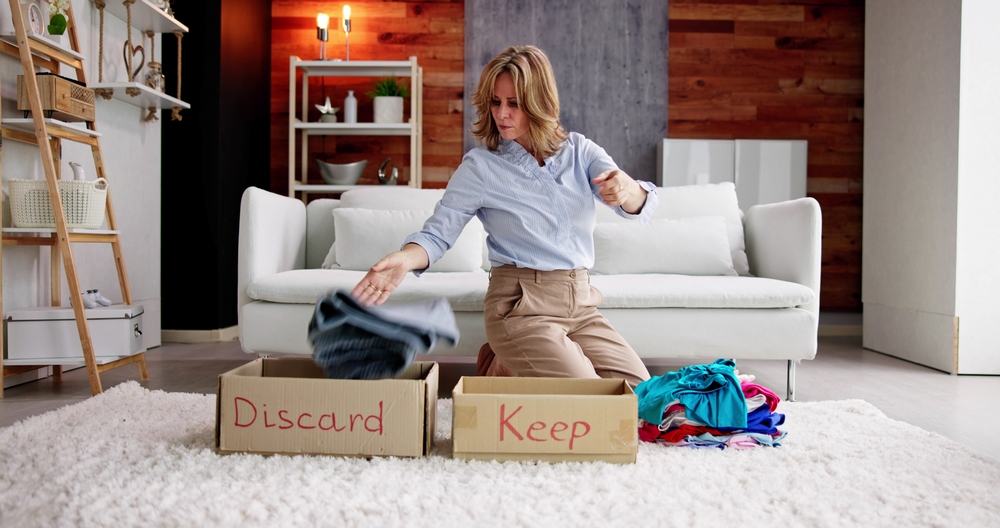Woman kneeling on floor and separating clothing into Discard and Keep boxes