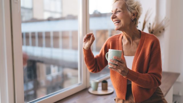 Stylish senior woman laughing wearing orange cardigan with coffee mug