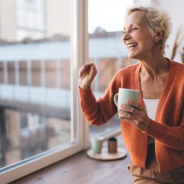 Stylish senior woman laughing wearing orange cardigan with coffee mug