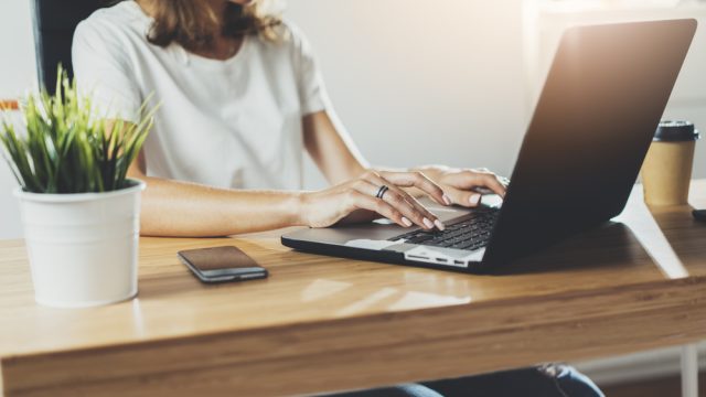 Woman working from home on laptop at desk with plant