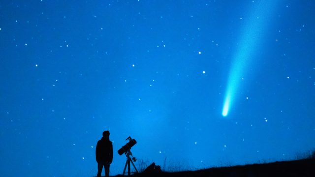 A person stargazing and watching a comet with a long tail in the night sky