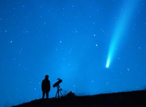 A person stargazing and watching a comet with a long tail in the night sky