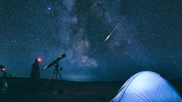 A person standing near a tent and telescope while watching a meteor shower at night