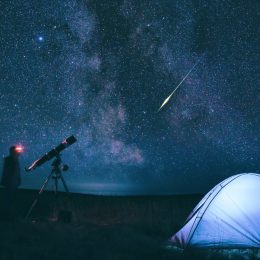 A person standing near a tent and telescope while watching a meteor shower at night