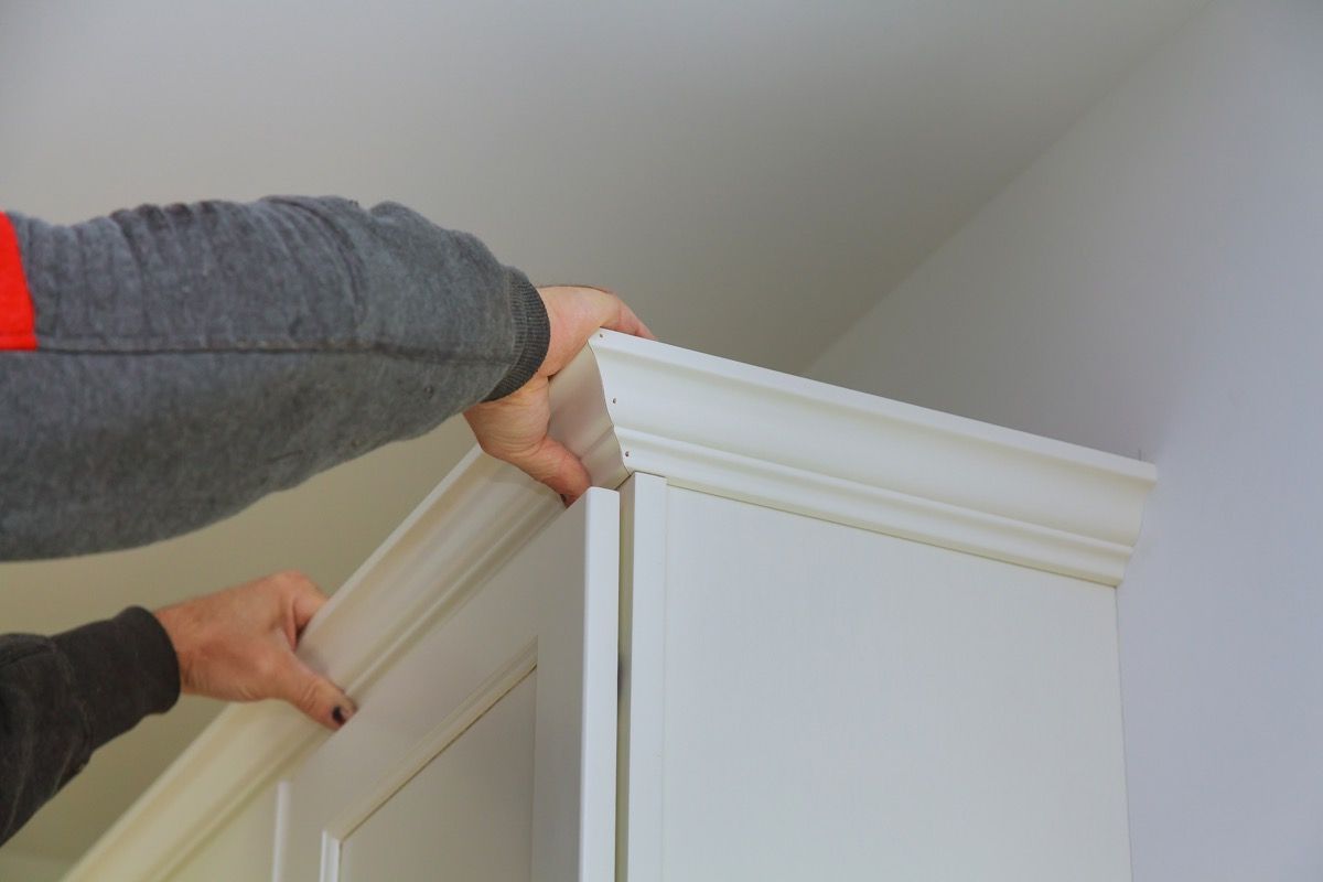 carpenter using nail gun to add crown moulding on cabinets