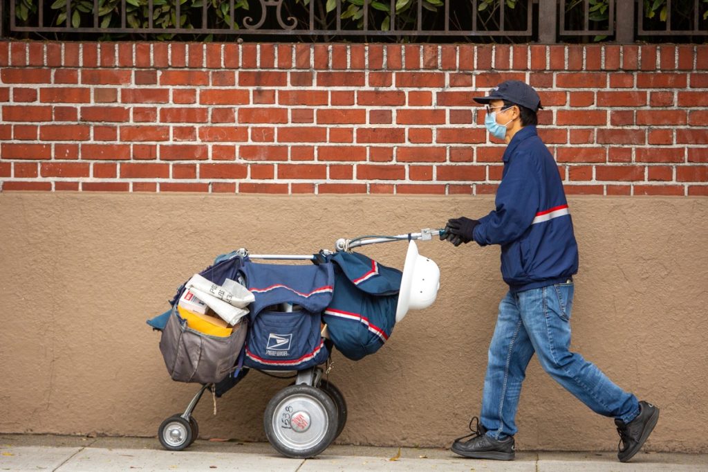 San Francisco postal worker in mask delivering mail during stay-at-home order.