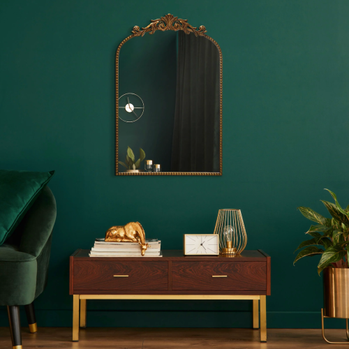 Styled product shot of a gold mirror from Walmart, set on an emerald green wall 