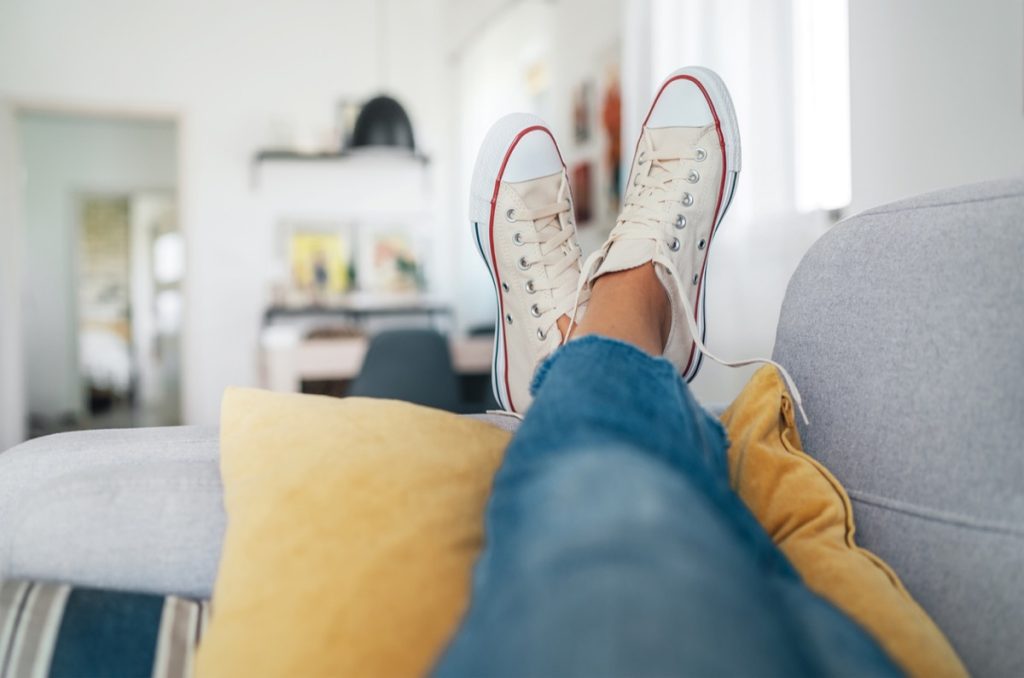 Close up on woman's feet in casual sneaks propped up on couch