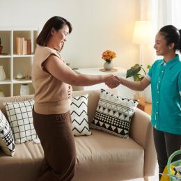 woman shaking hands with cleaning service worker to thank her for her work while they standing in living room
