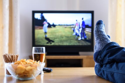 Close up of someone's feet on their coffee table while they watch golf on TV with snacks and a beer